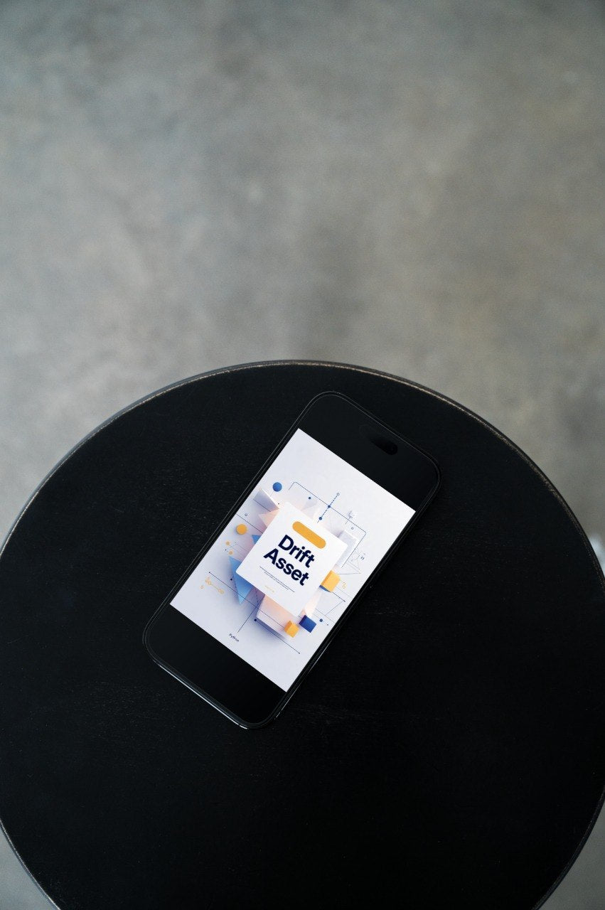 A black smartphone lying on a round black table, displaying the DRAFT ASSET app on its screen against a gray concrete-textured background.